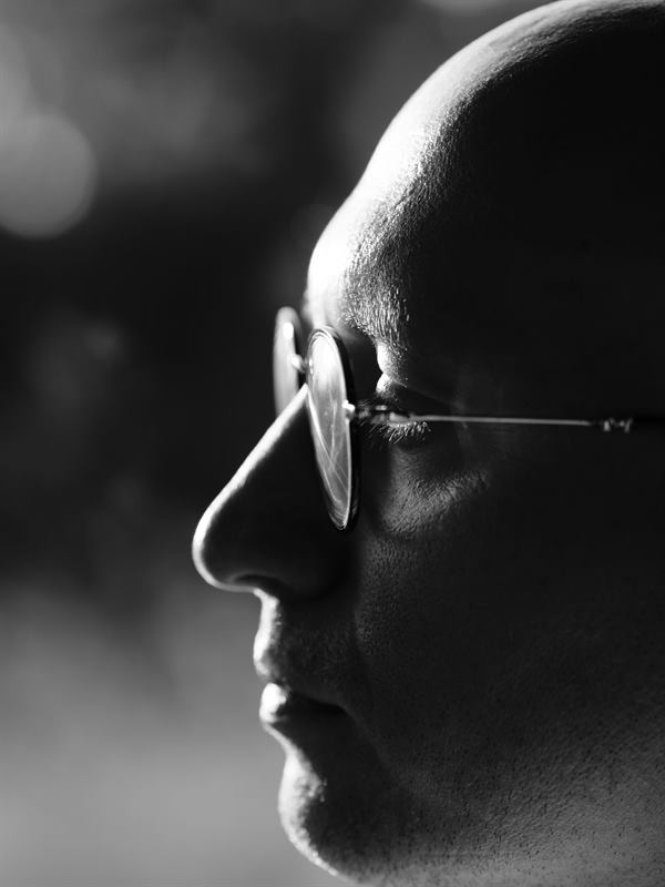A close profile portrait in black and white, thin glasses catching the light