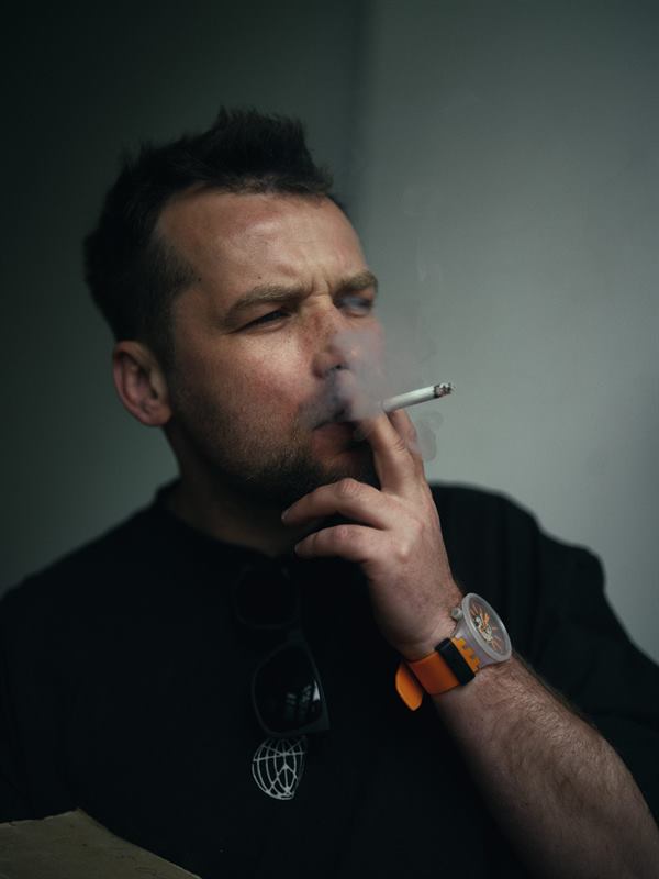A man smoking a cigarette in a doorway, eyes narrowed against the smoke