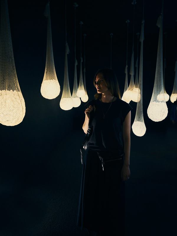 A woman standing among hanging teardrop lamps in a dark room