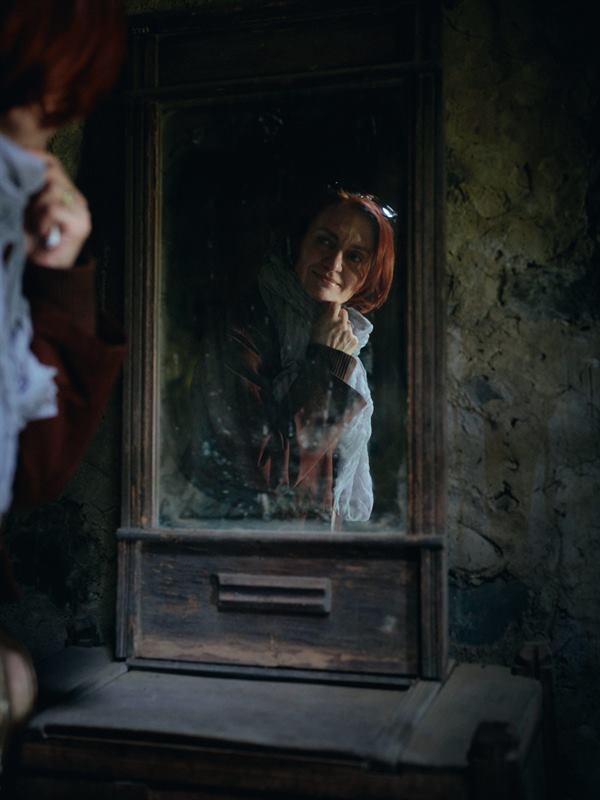 A woman reflected in a mirror propped against a peeling wall