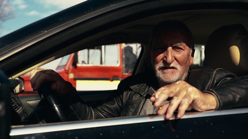 An older man leaning out of the window of a parked car