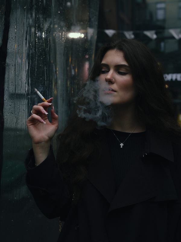 A woman smoking behind a rain-streaked window at night