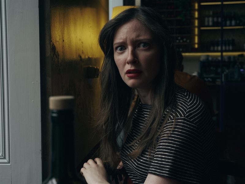 A woman in a striped top in a bar, caught mid-sentence