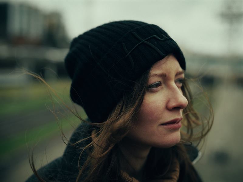 A close portrait of a woman in a black beanie, hair blown across her face