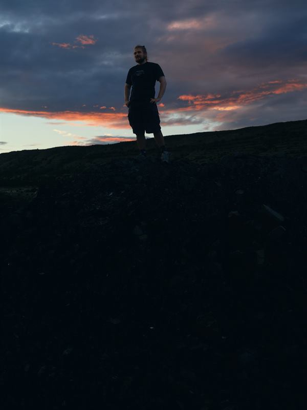 A figure standing on a dark ridge against a streaked evening sky
