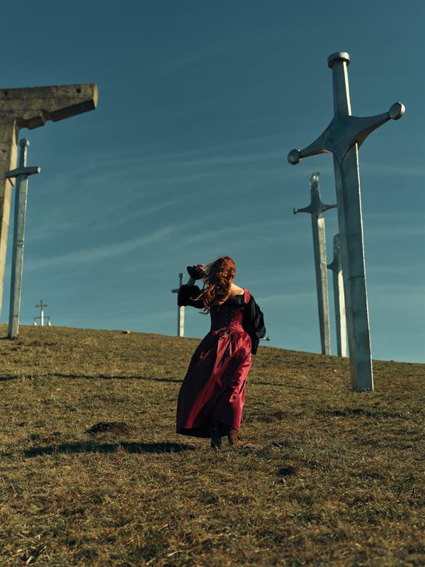 A woman in a red dress on a hillside among tall steel crosses