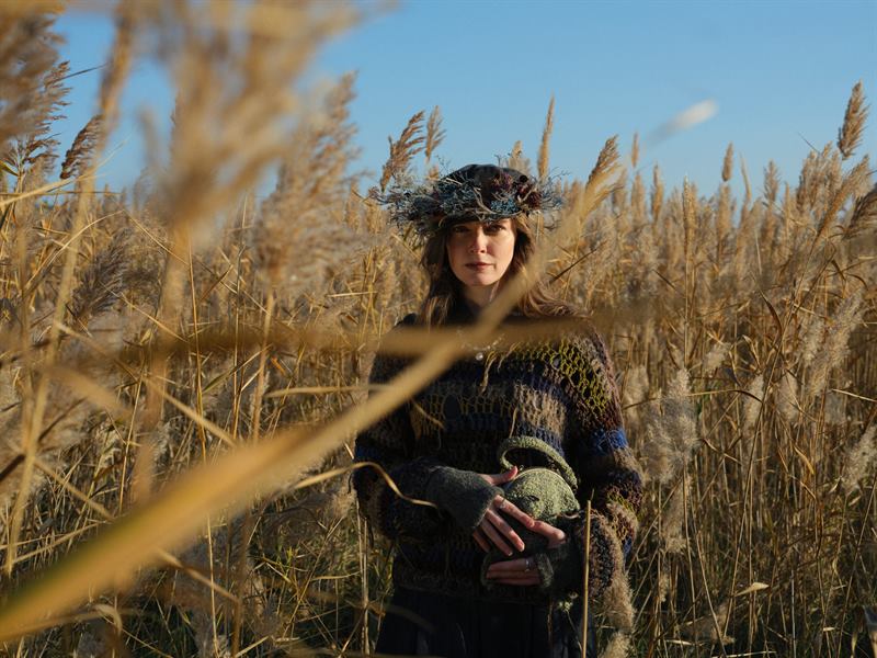 A woman in a flower crown among pale reeds in low sun