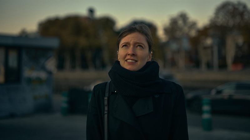 A woman in a dark coat on an empty street, looking up
