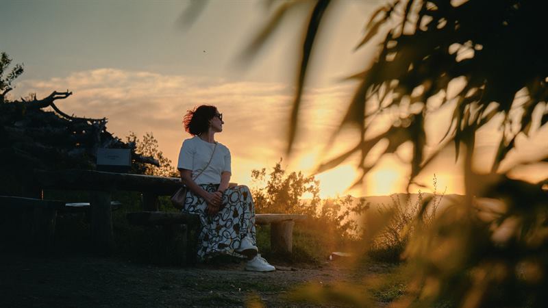A woman on a bench watching the sun go down through leaves