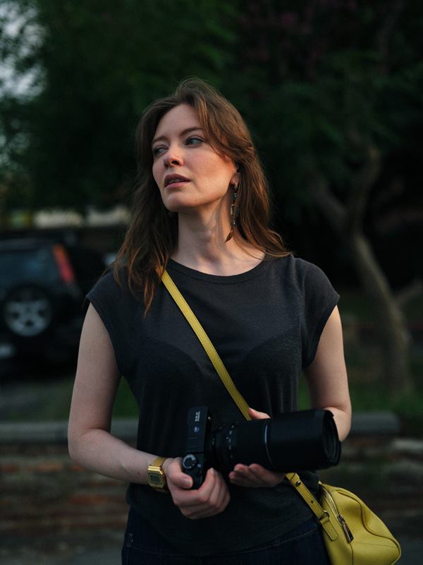 A young woman with a camera on a strap, standing in a street