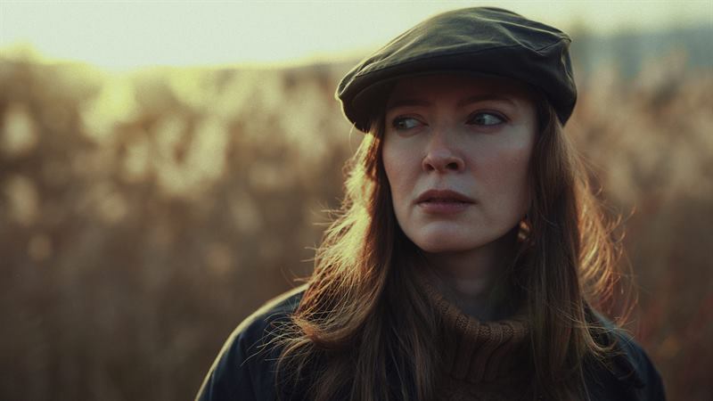 A close portrait of a woman in a flat cap in golden backlight