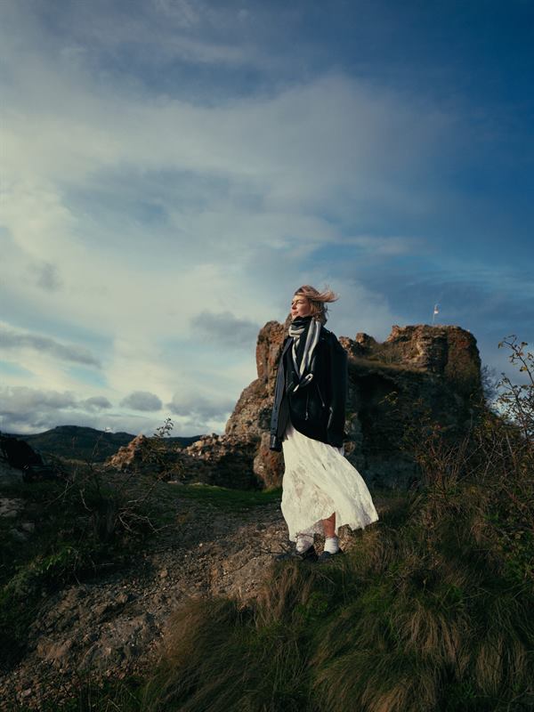 A woman in a white skirt standing on a rock outcrop under a wide sky