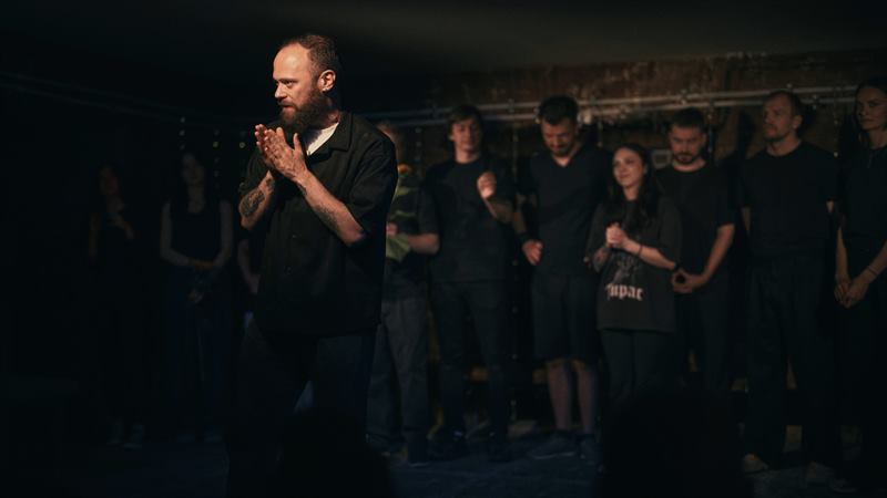 A man applauding in front of a line of people dressed in black