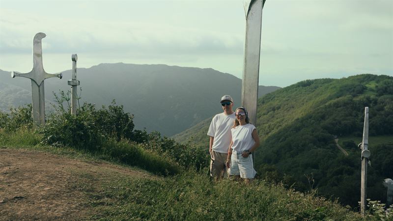A couple standing by a monument on a green ridge above a gorge