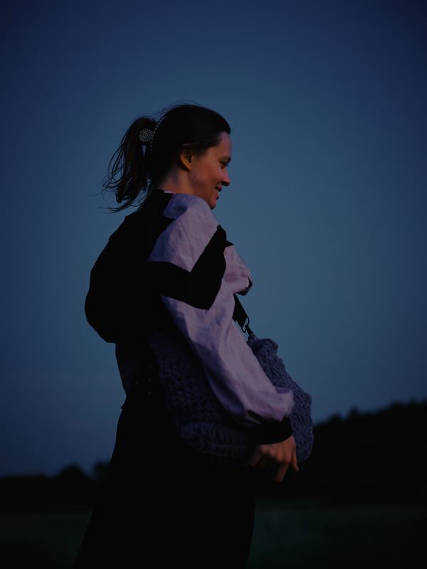 A woman in a pale shirt turning to look back, laughing, against a deep blue dusk sky