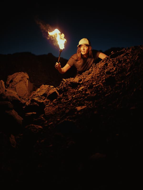 A woman with a raised torch climbing over broken rock, the flame lighting the stones around her