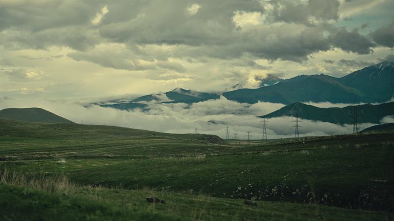 Power lines running across a green plateau under a heavy sky