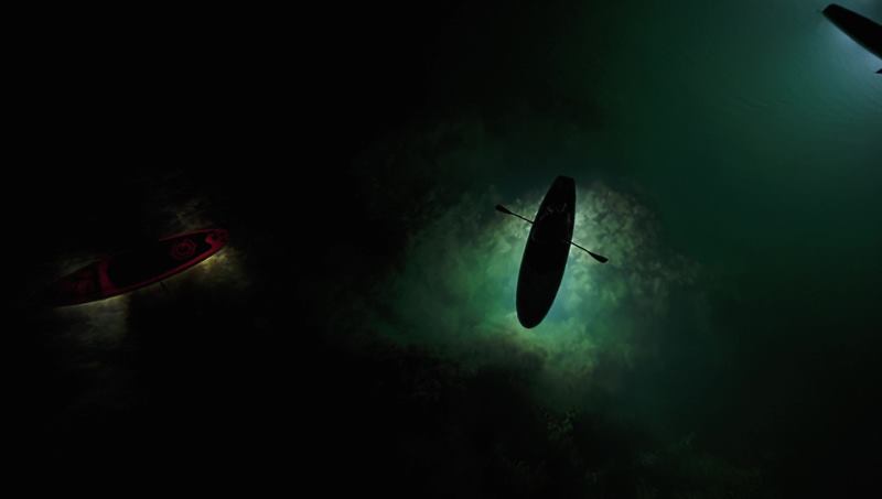A boat lit from below in dark green water at night