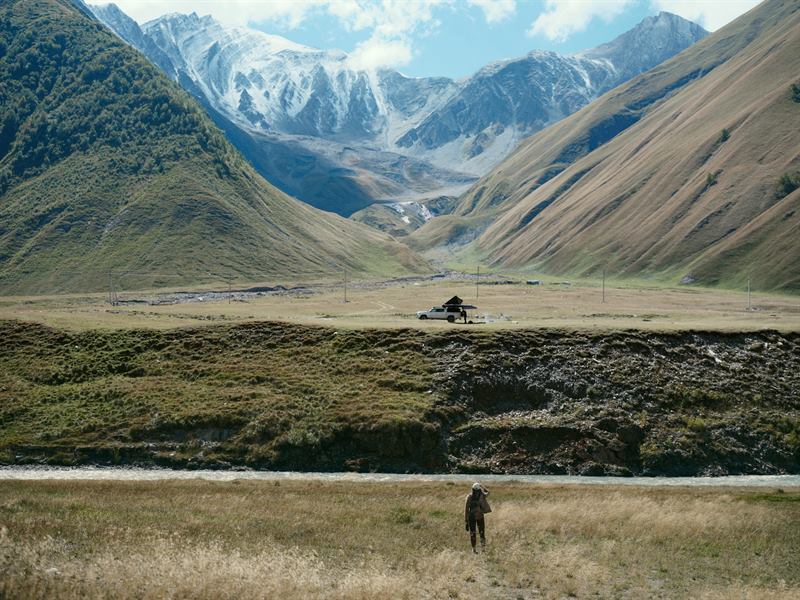 A walker crossing dry grass below a snow-capped range