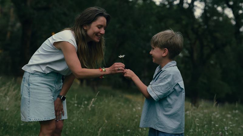 A woman handing a small flower to a boy in a summer meadow
