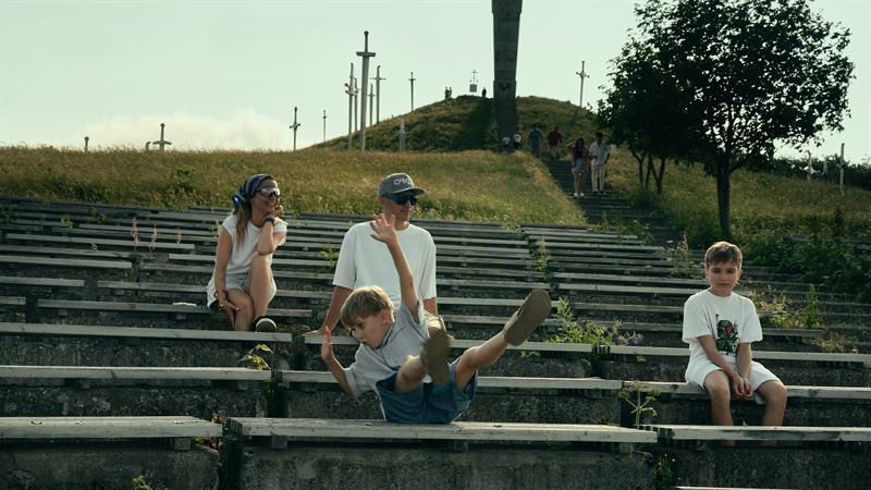 A family sitting on wide concrete steps below a hilltop monument