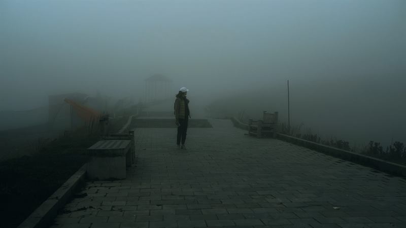 A figure walking a promenade in thick fog