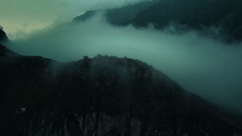 Cloud pouring over a dark forested ridge