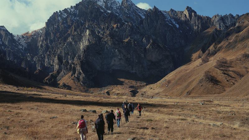 A line of walkers crossing a valley below jagged peaks