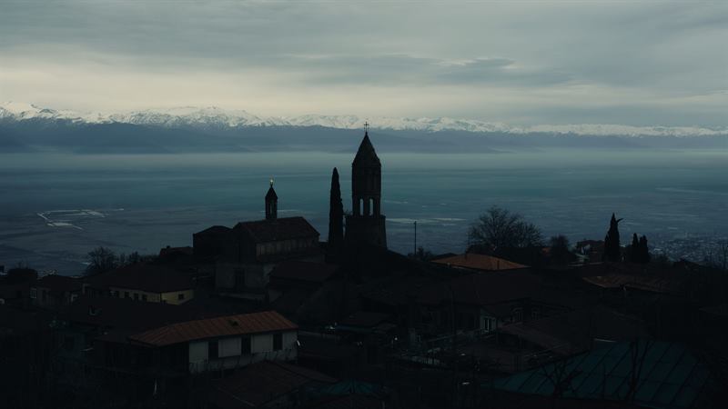 A church tower over village roofs with a snow range behind