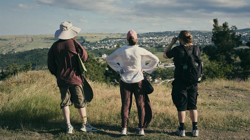 Three hikers looking out over a city from a grassy hilltop