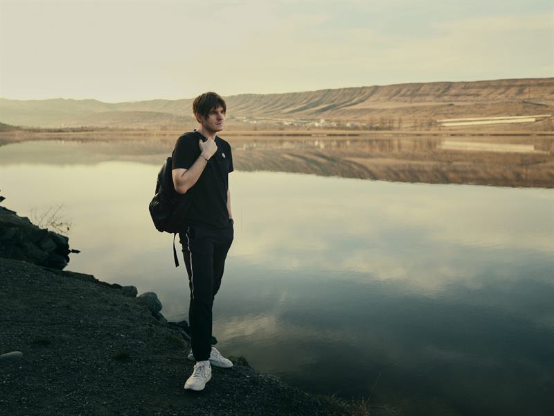 A young man with a backpack at the edge of a still lake