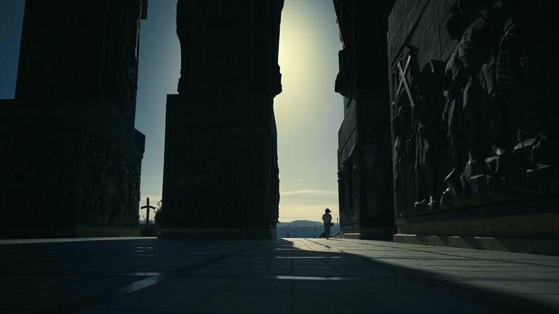 A monumental arch with a small figure walking into the light