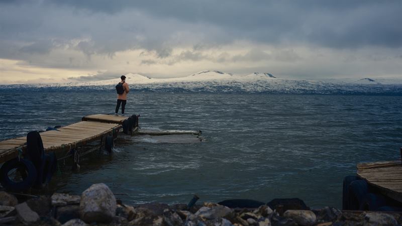 A person standing at the end of a wooden pier on a rough sea