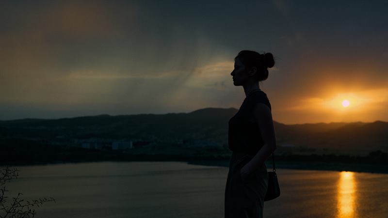 A woman in silhouette by a lake at sunset