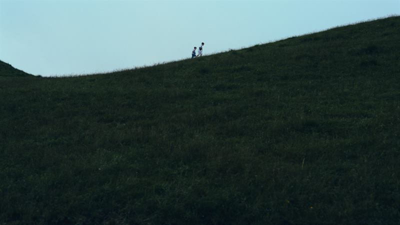 Two tiny figures on the crest of a green hill