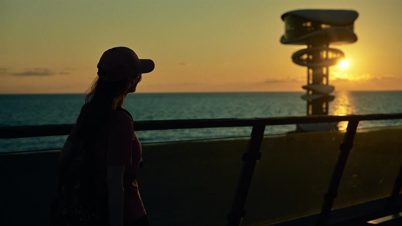 A traveller at a seafront railing at sunset in Anaklia, the spiral tower standing in the low sun