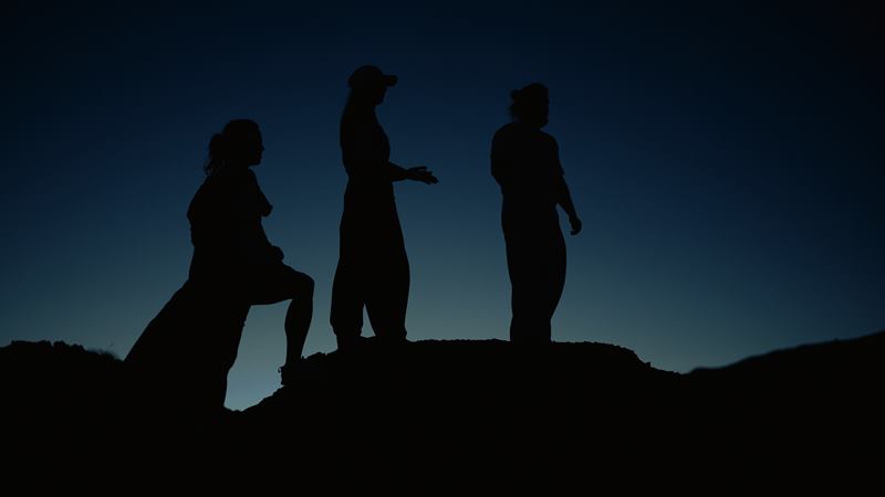 Three friends in silhouette on a ridge against the blue gradient of late dusk