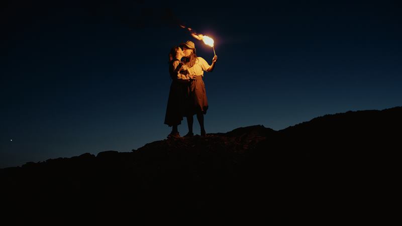 A couple kissing on a ridge at night, a burning torch held up above them